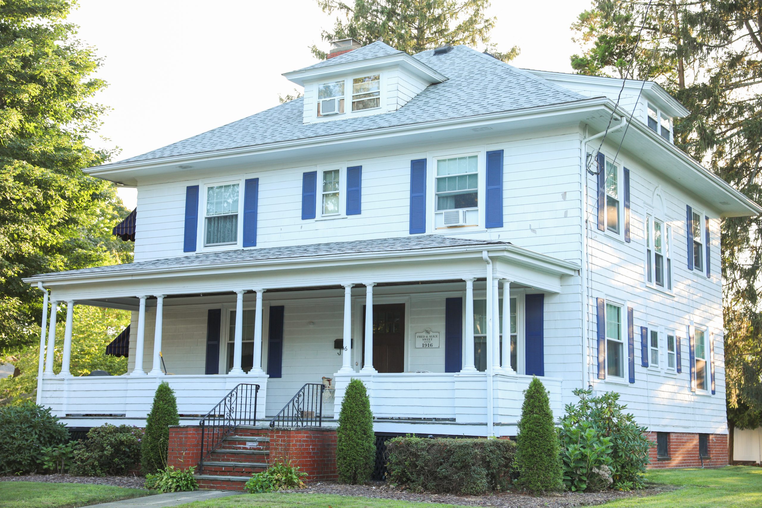 A home with a large front porch, white siding, blue shutters, and gray shingle roofing.