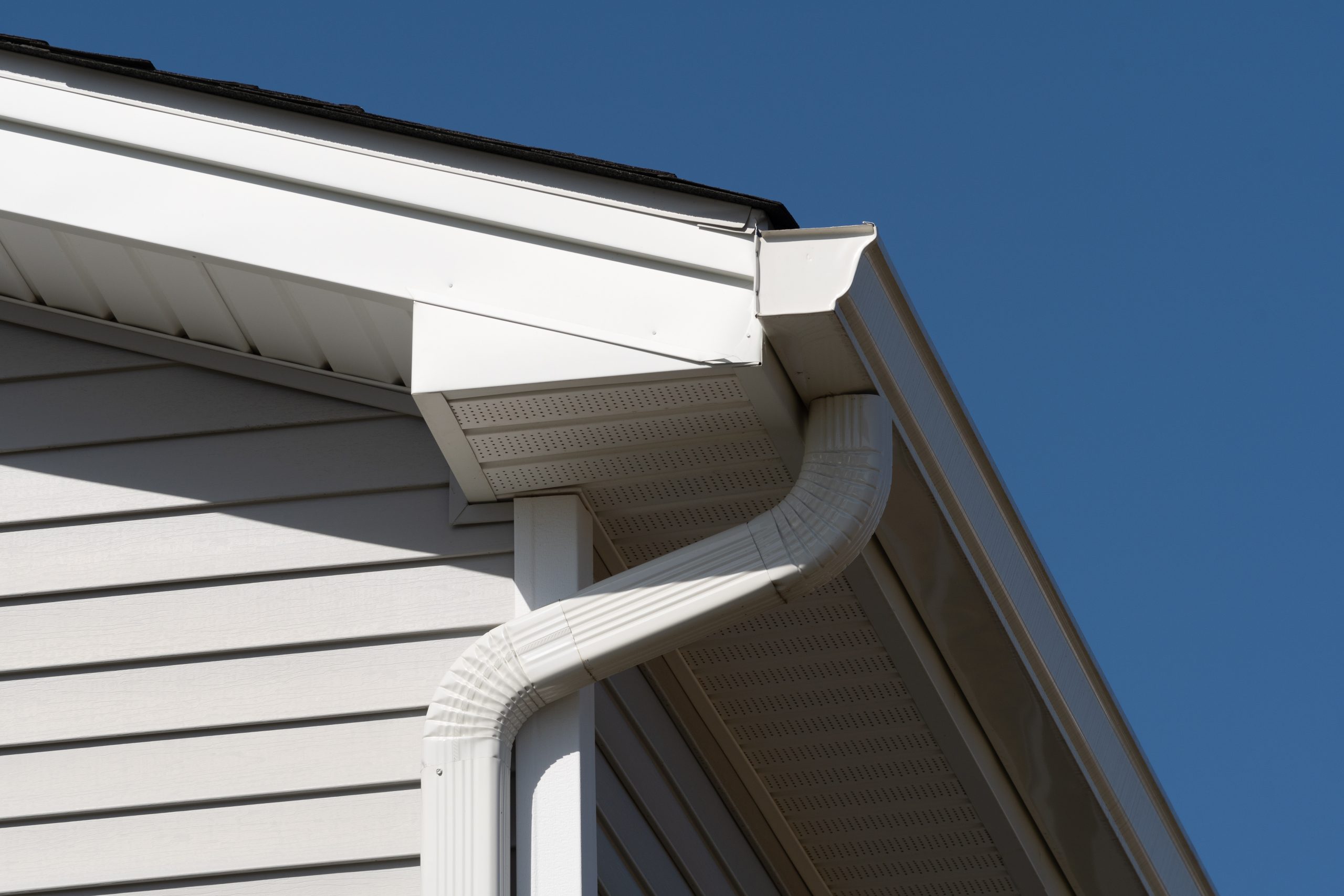 The corner of a home with gray siding, white trim, and white seamless gutters.