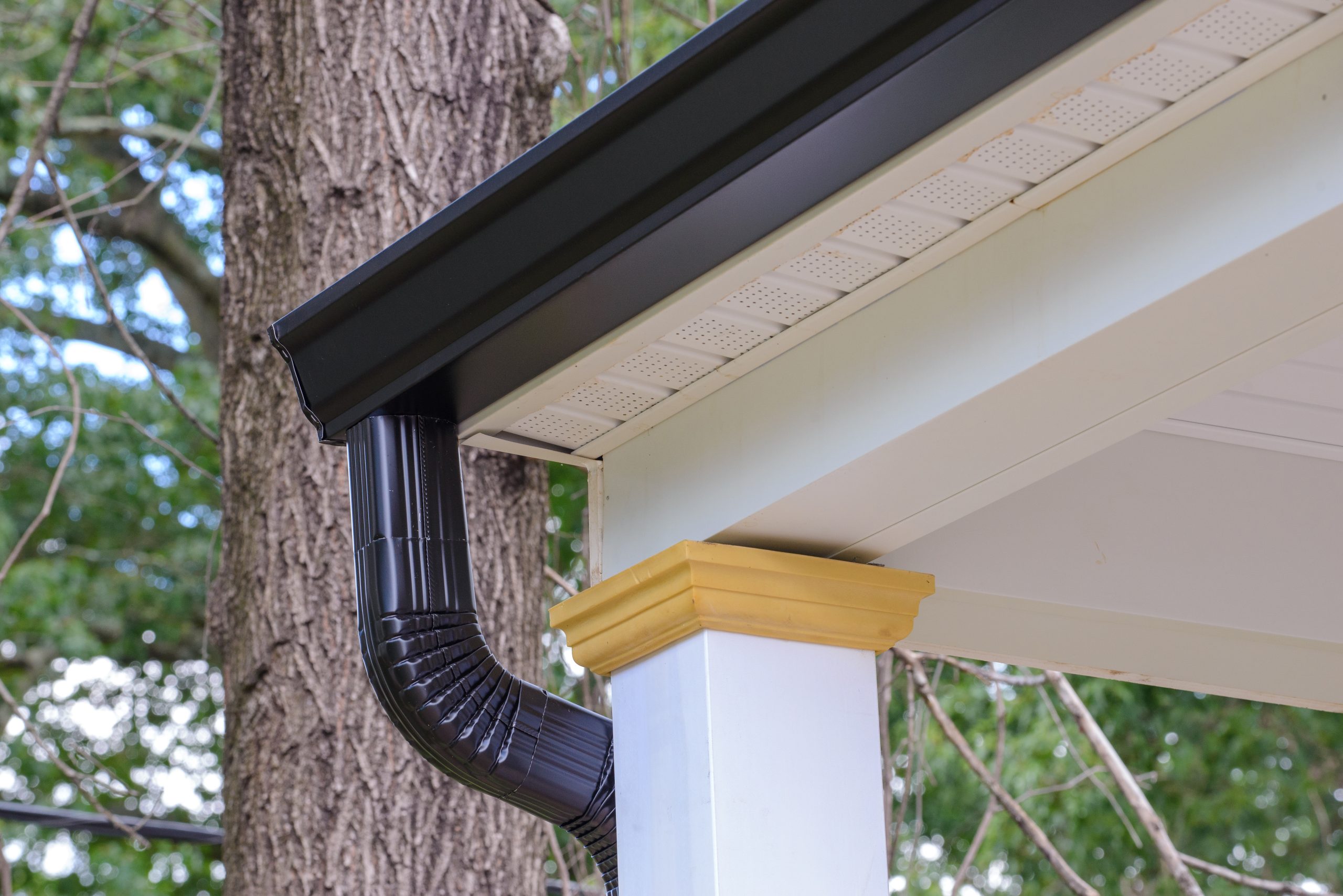 Black seamless gutters and downspout on the corner of a porch with a large pillar.
