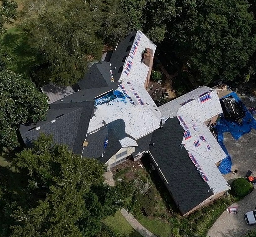 Drone view of a commercial roof replacement in progress, showing the underlayment exposed to the right and the newly installed shingles to the left.