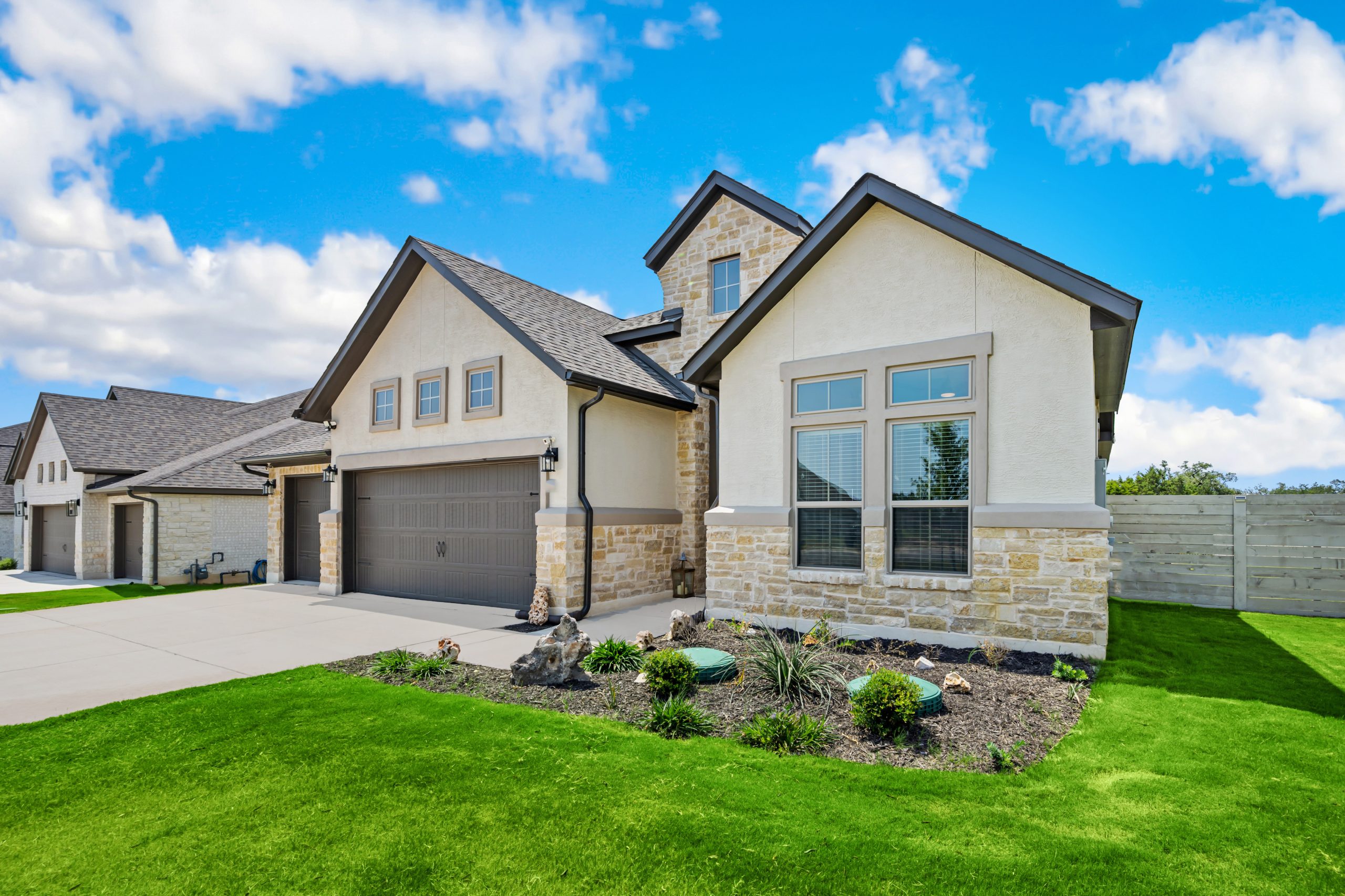 Exterior of a home with tan stucco and stone accents and a shingle roof.