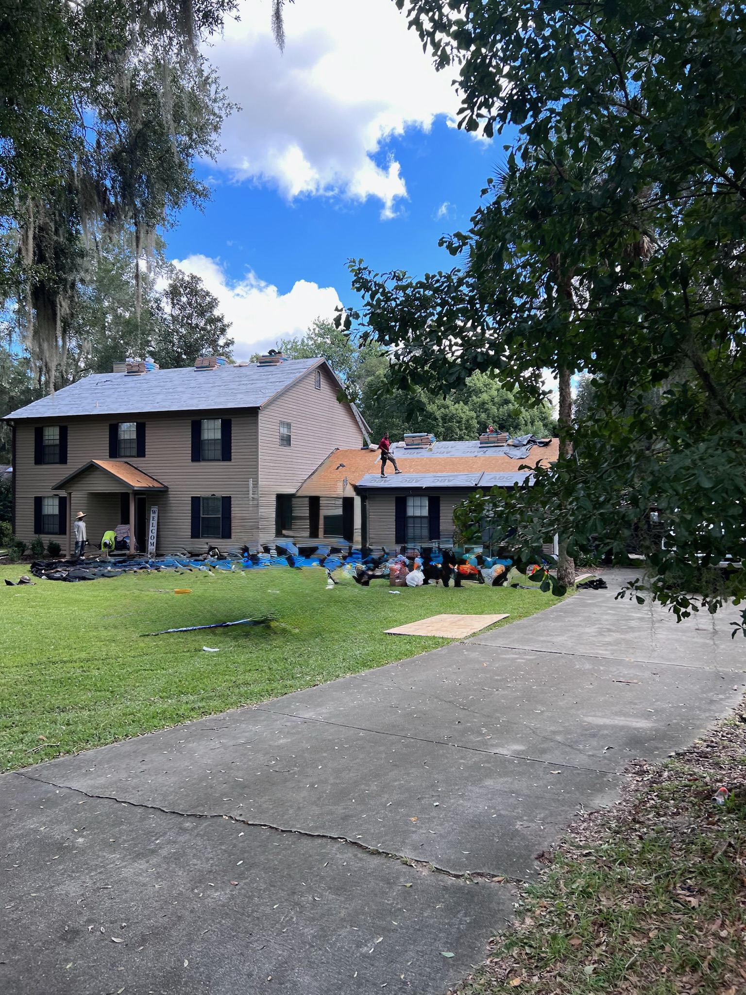 Distant view of a residential roof replacement in process, with the yard protected with blue tarps.