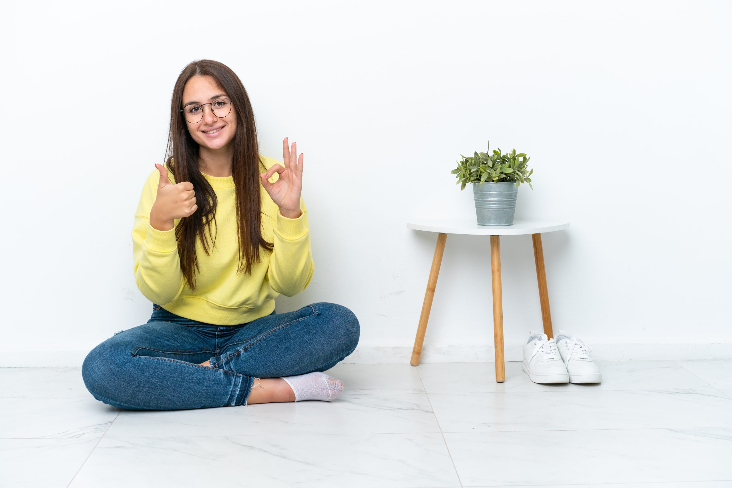 A woman sitting on the floor giving a thumbs up and “ok” signal with her hands.