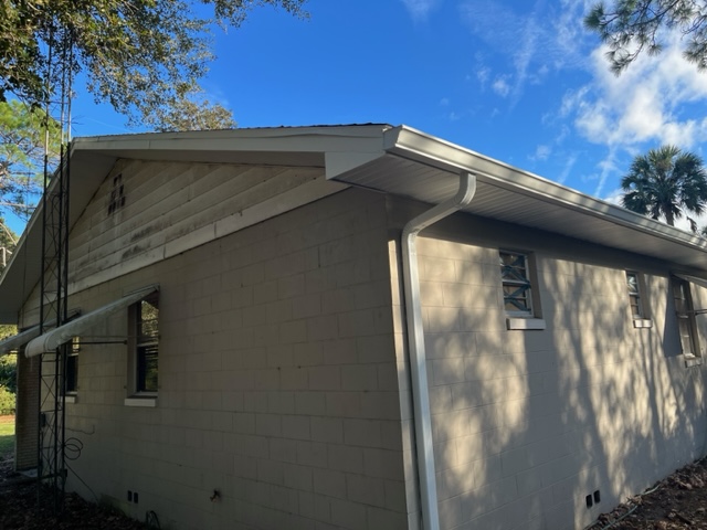 An upward look at the corner of a white brick house with white soffit, fascia, and gutters under a blue sky.
