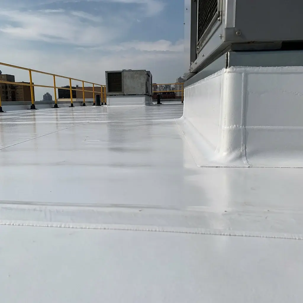 Resounding Commercial Roof Repair In Alachua, FL | Sentinel Roofing A close-up of the roof of a building covered in shiny white roofing material. Various metal equipment and fencing can be seen on different parts of the roof, and there are more buildings visible in the distance.