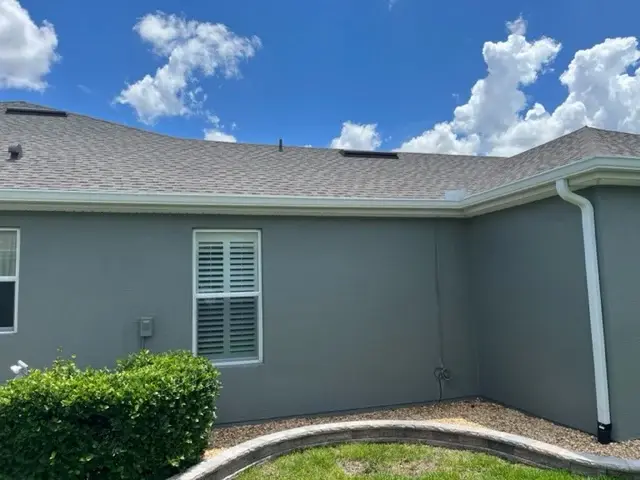 Responsive Gutters In Alachua, FL | Sentinel Roofing A home with a blue-gray exterior has a brown shingled roof and a white gutter system.