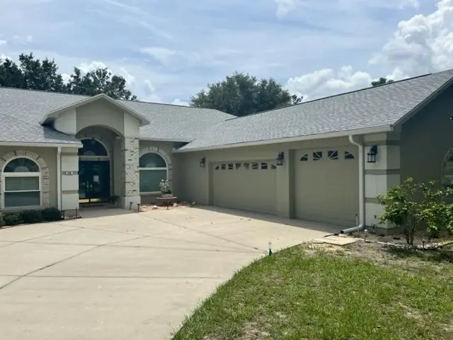 Restored Gutters In Alachua, FL | Sentinel Roofing A photo taken from the driveway and showing the front of a home with a gray-green exterior, a light gray shingled roof, and white seamless gutters and downspouts.