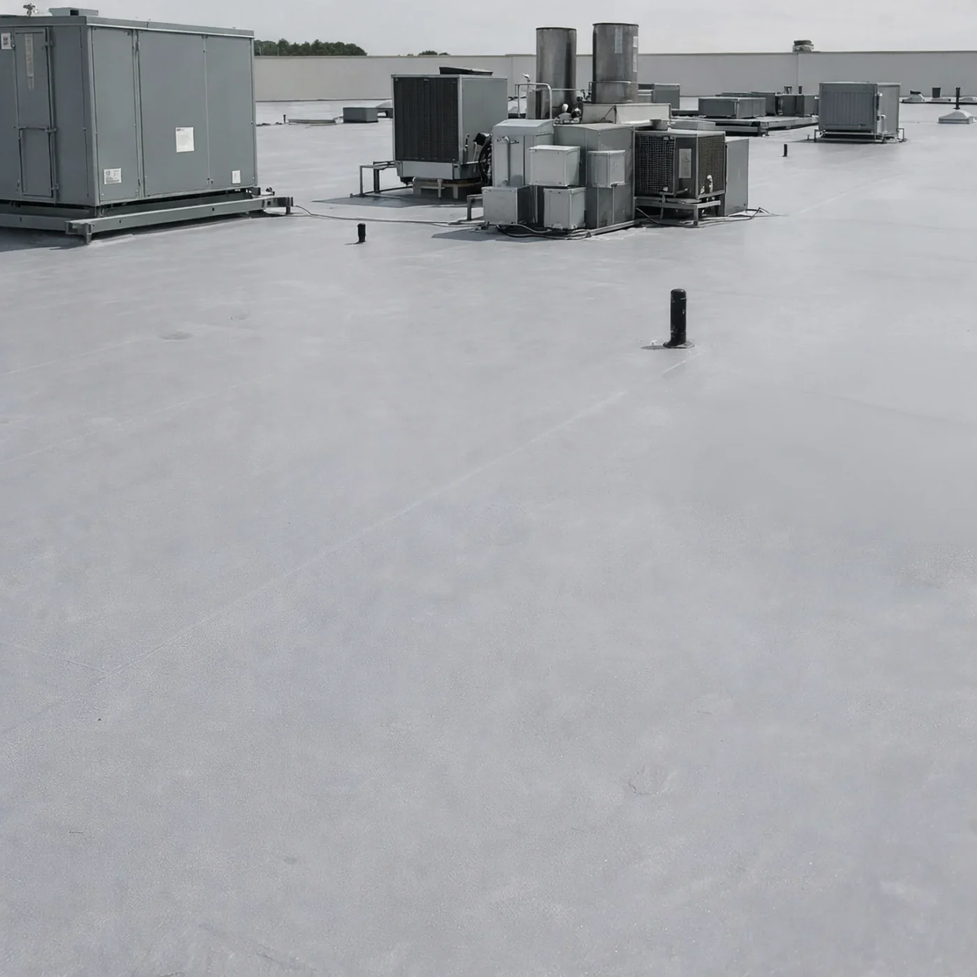 Seamless Commercial Roofing In Newberry, FL | Sentinel Roofing A close-up of a flat roof with a light gray surface. There are multiple pieces of silver machinery visible on the far side of the roof, along with vent pipes and a high wall around the edge.