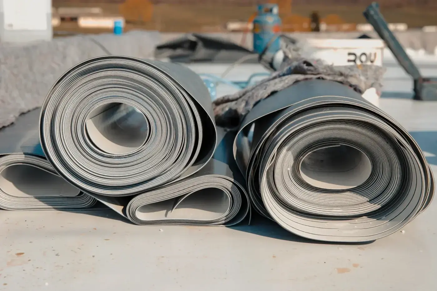 Smart Commercial Roof Repair In Gainesville, FL | Sentinel Roofing Two rolls of white roofing material are lying on a flat rooftop that’s in the middle of commercial roofing work. Behind them, various roofing materials can be seen.
