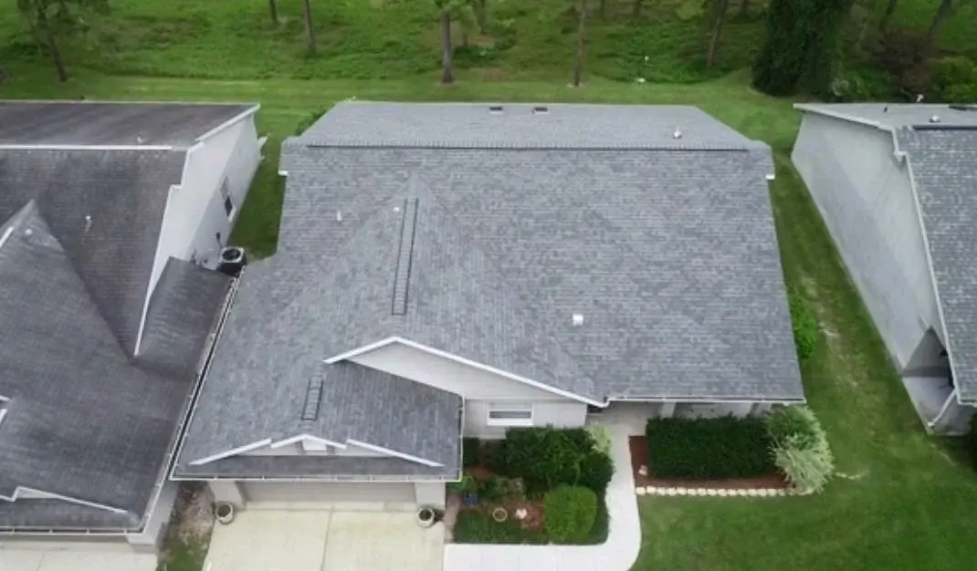 Spectacular Residential Roof Repair In Alachua, FL | Sentinel Roofing Two homes, side-by-side, as seen from a drone photo. The home on the right has a light gray shingled roof, which looks new. The home on the left also has a gray shingled roof, but it looks older, and the shingles are darker.